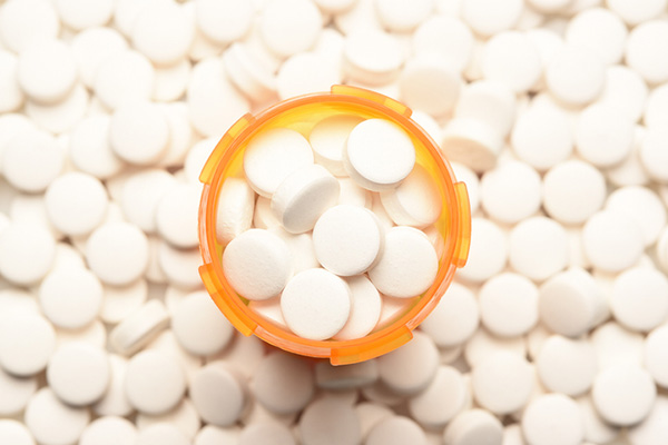 Prescription bottle filled with pills, surrounded by more of the same tablets